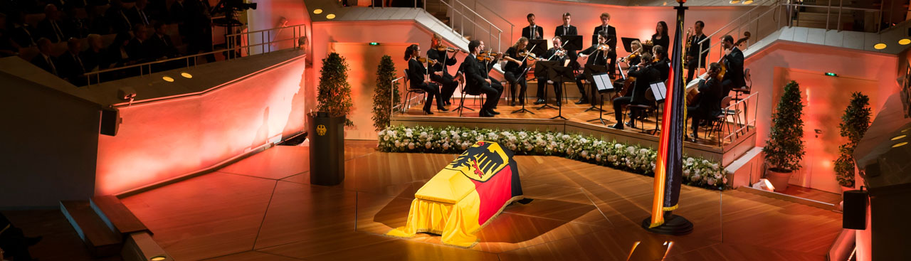 Der Sarg des Bundespräsidenten a.D. Walter Scheel ist in der Berliner Philharmonie aufgebarrt und mit der Bundesdienstflagge bedeckt. Im Hintergrund sind die Musiker Orchester-Akademie der Berliner Philharmoniker  zu sehen.